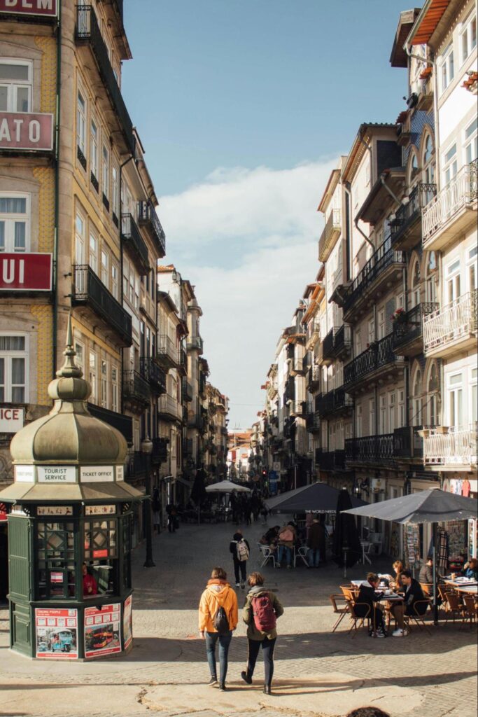 Two people walking down a narrow, cobbled street in Porto, surrounded by traditional Portuguese architecture.