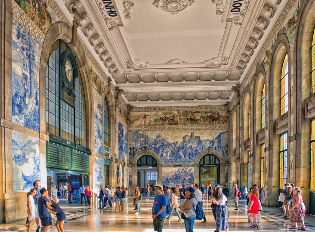 Busy scene inside São Bento Station in Porto, with travelers and commuters amidst the stunning azulejo tile murals.