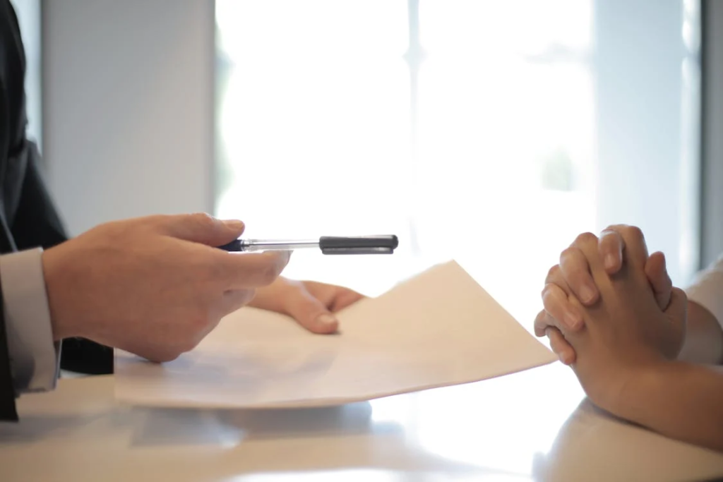 Close-up of two hands with a pen poised to sign an insurance contract on a paper document.